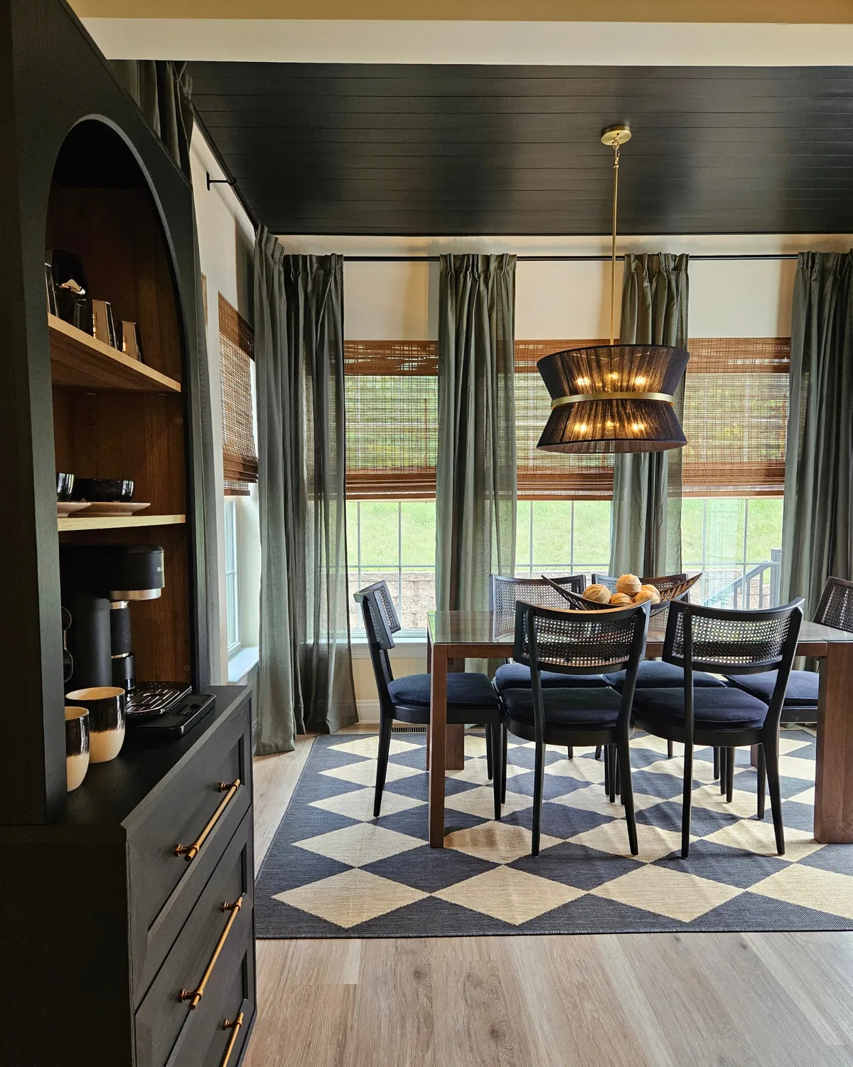 Dining room seen past a black arched hutch styled as a coffee bar, with sage linen curtains and woven shades at the windows