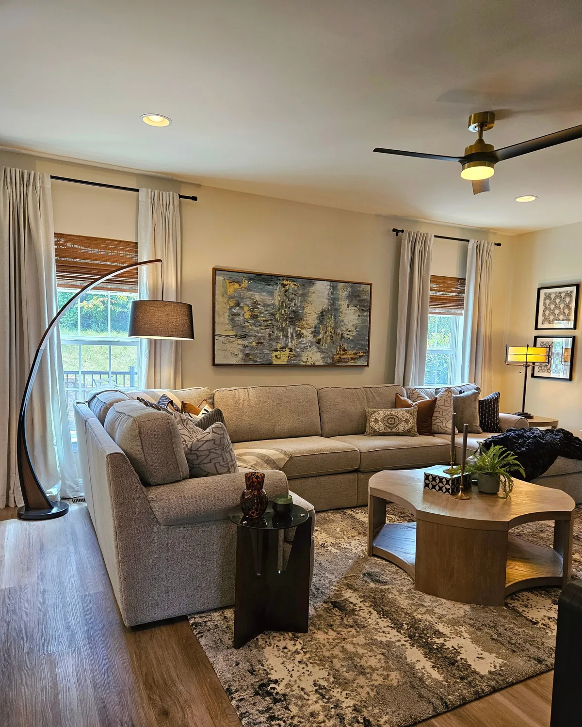 Living room with a cream sectional, arc floor lamp, abstract painting and a sculptural wood coffee table on a gray patterned rug