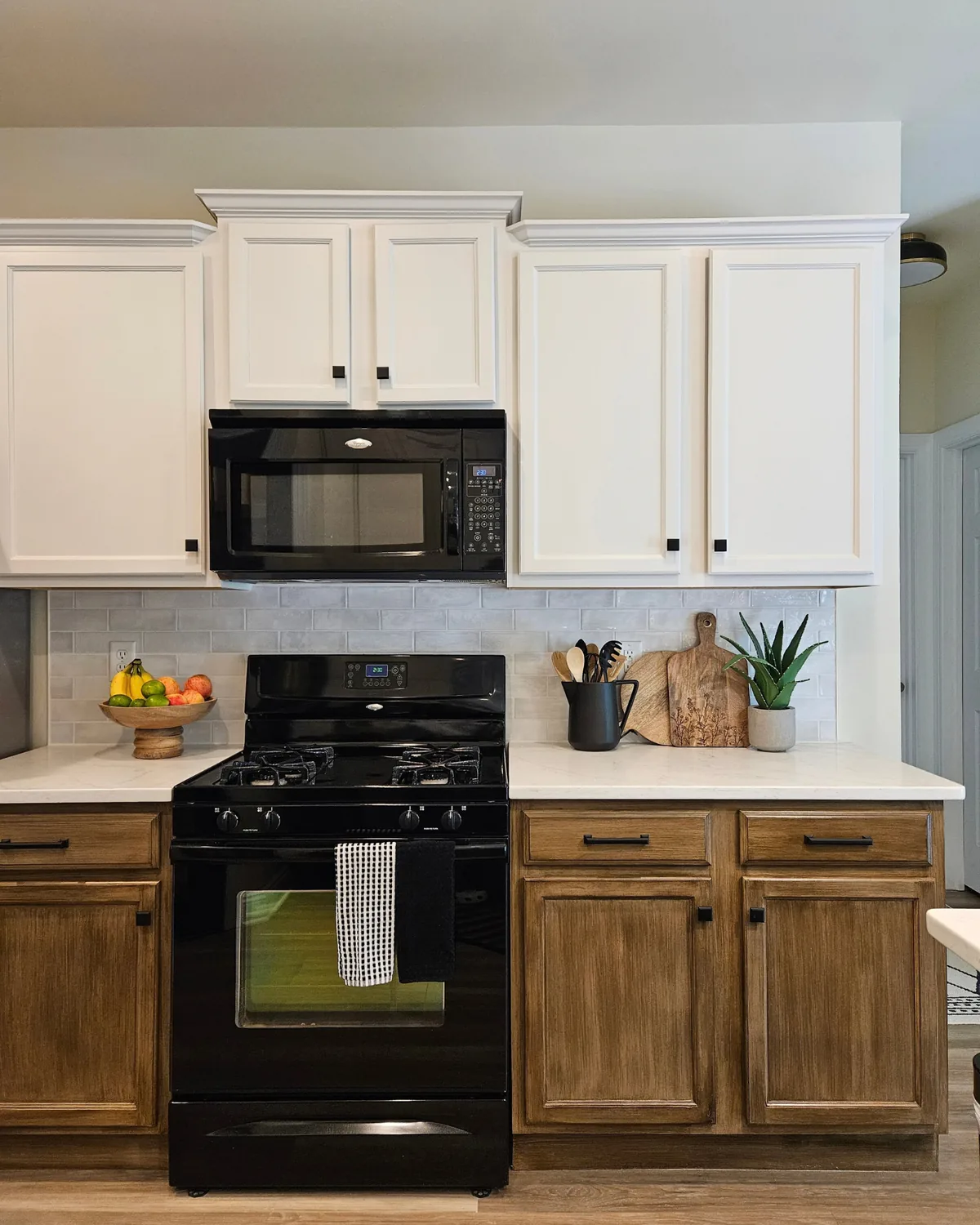 Kitchen with white upper cabinets, stained wood lowers, a black range and a styled counter with fruit and a cutting board