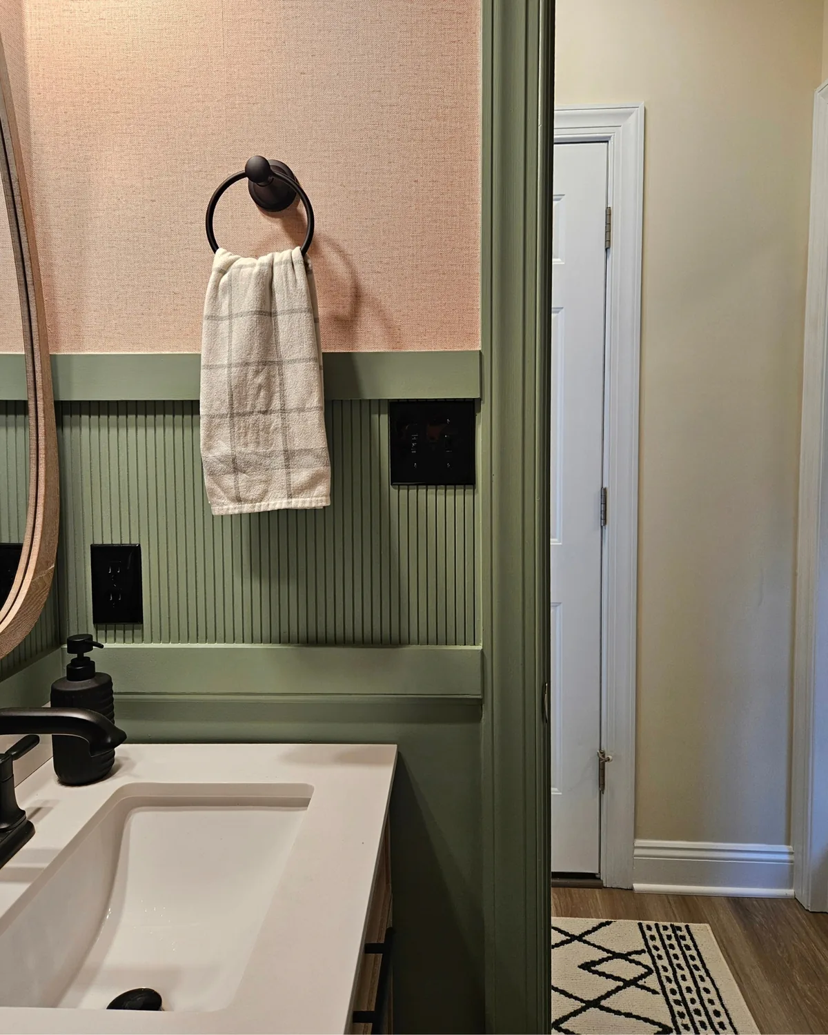 Close-up of the powder room's sage beadboard, black towel ring and white vanity against blush walls