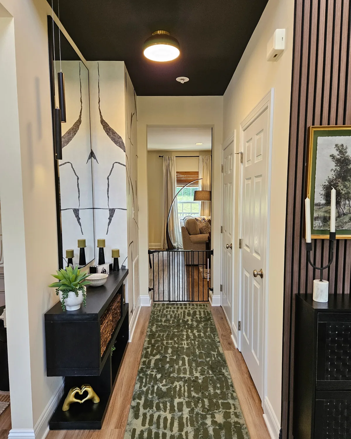 Long hallway with a black ceiling, a sculptural console and a green patterned runner, beside a dark wood-slat wall