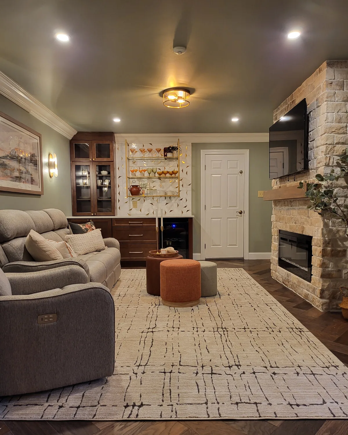 Bonus room in soft sage with recliners, a plaid rug, a whitewashed brick fireplace and the bar wall behind
