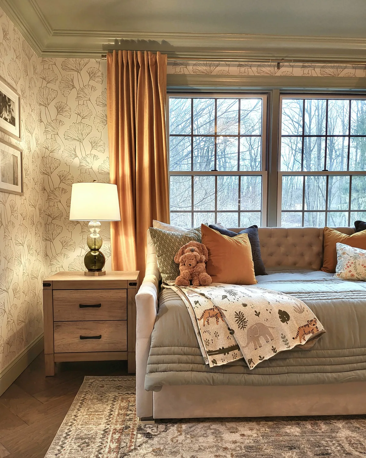 Daybed nook with amber velvet curtains, a tufted daybed piled with pillows and ginkgo-leaf wallpaper