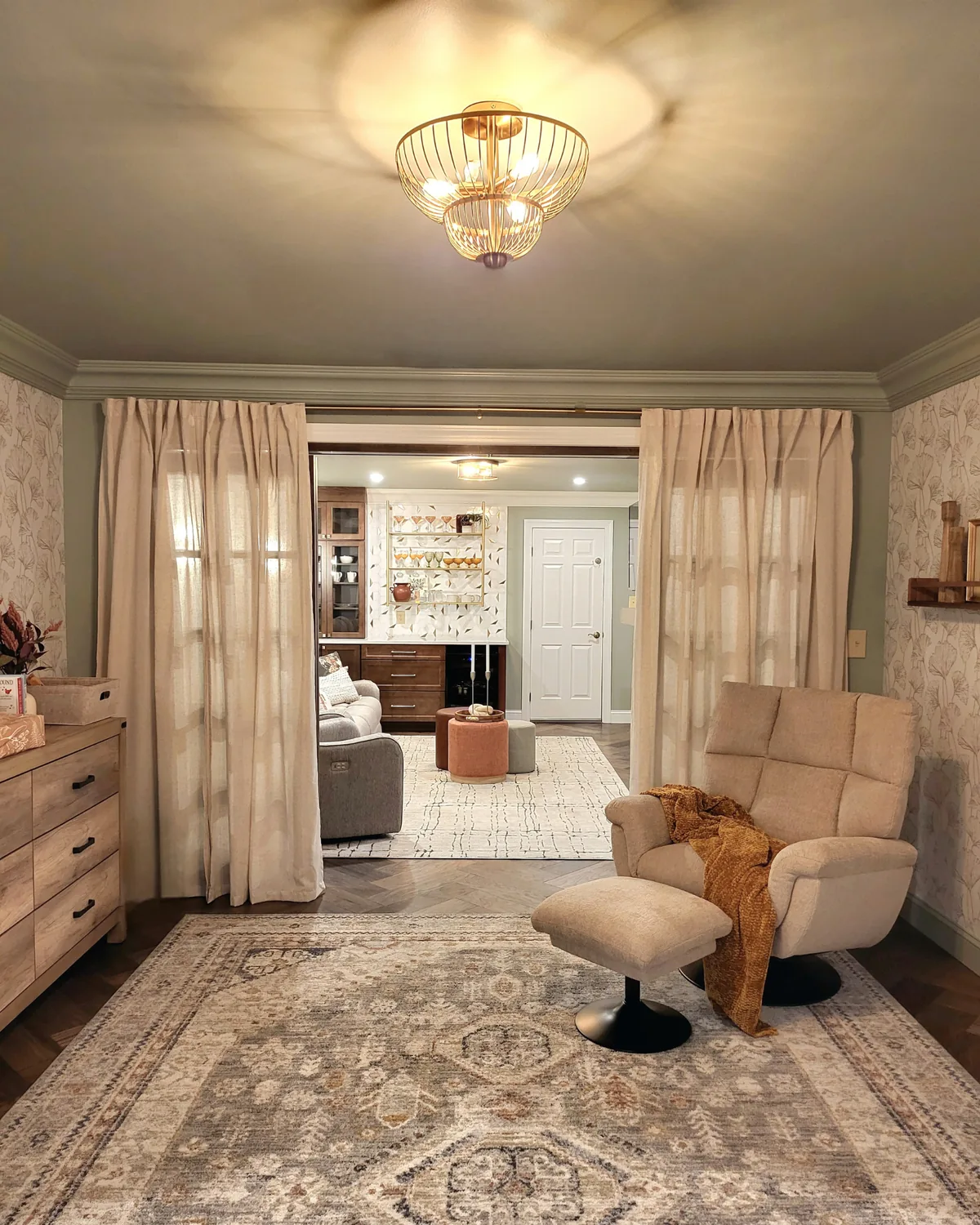 Reading corner with a swivel lounge chair and ottoman under a gold cage pendant, sheer curtains open to the bonus room