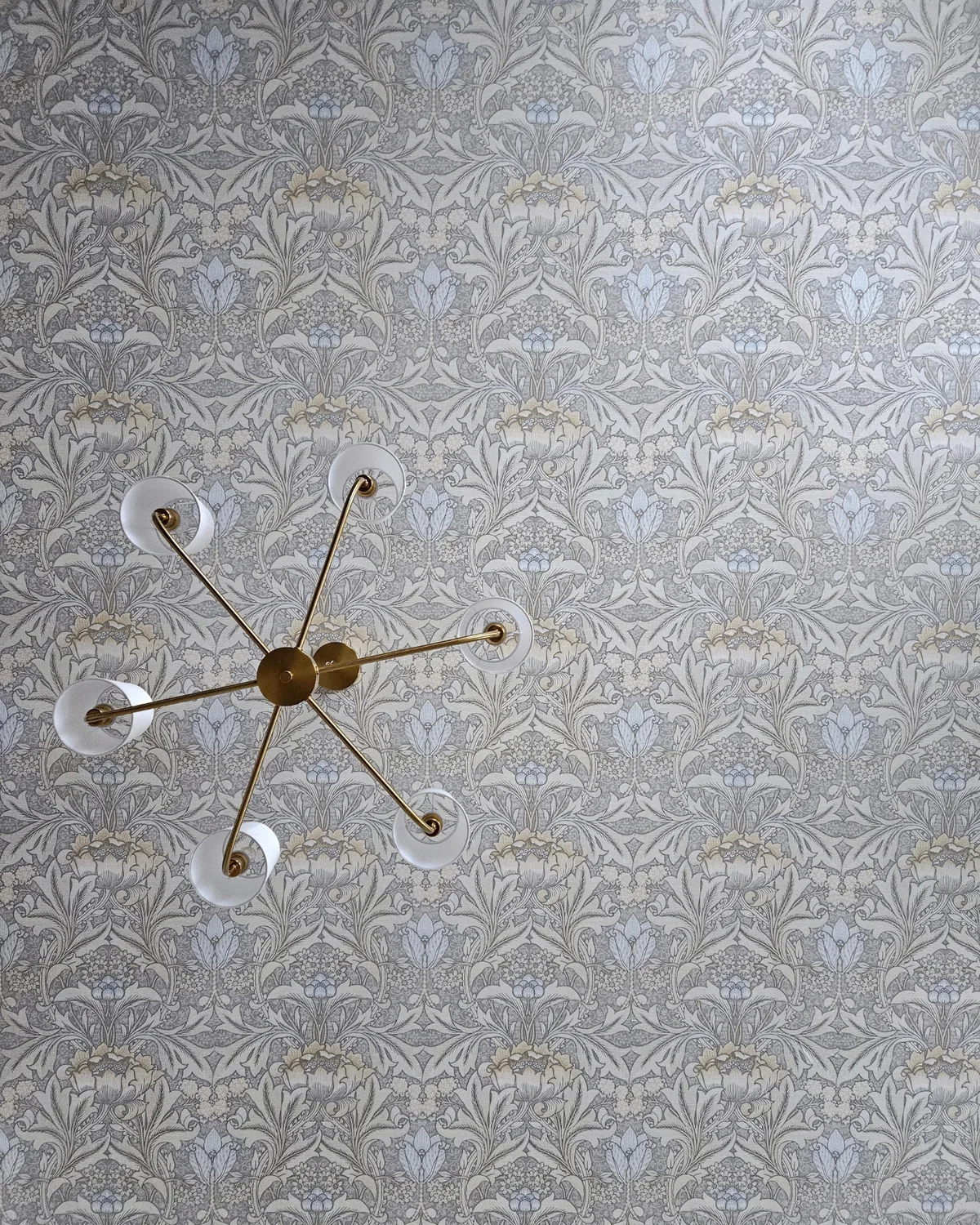 Looking up at the brass chandelier against the blue-and-cream botanical wallpapered ceiling