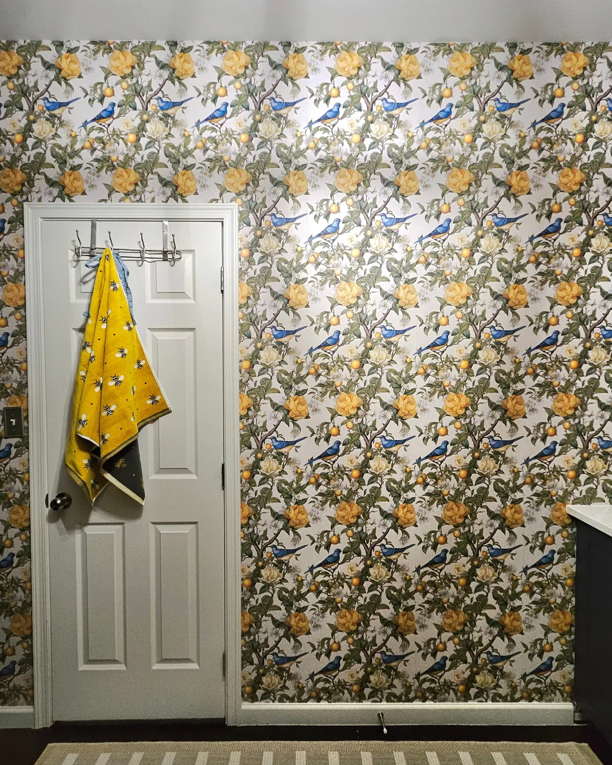 Pantry door wall covered in lemon-and-leaf wallpaper, with a yellow lemon-print towel hanging on the door