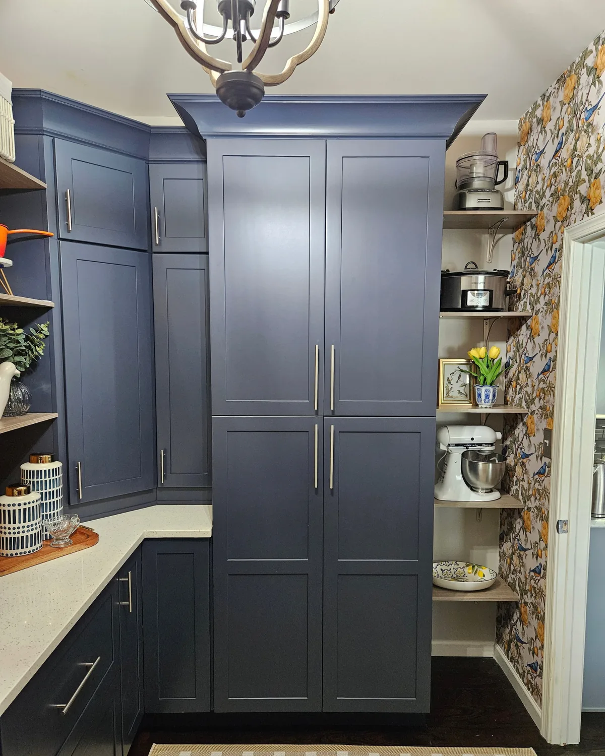 Tall navy pantry cabinets with brushed-nickel pulls under a lantern pendant, beside open shelves holding a stand mixer