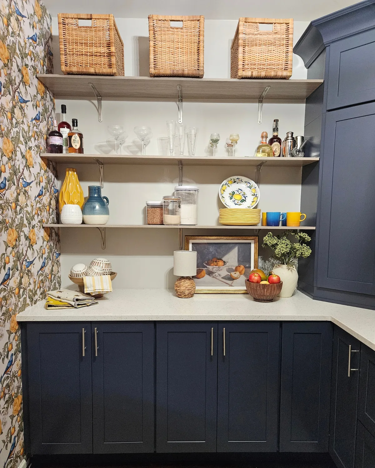 Wide view of the lemon wallpaper wall and open shelving with baskets, glassware and lemon plates above navy cabinets