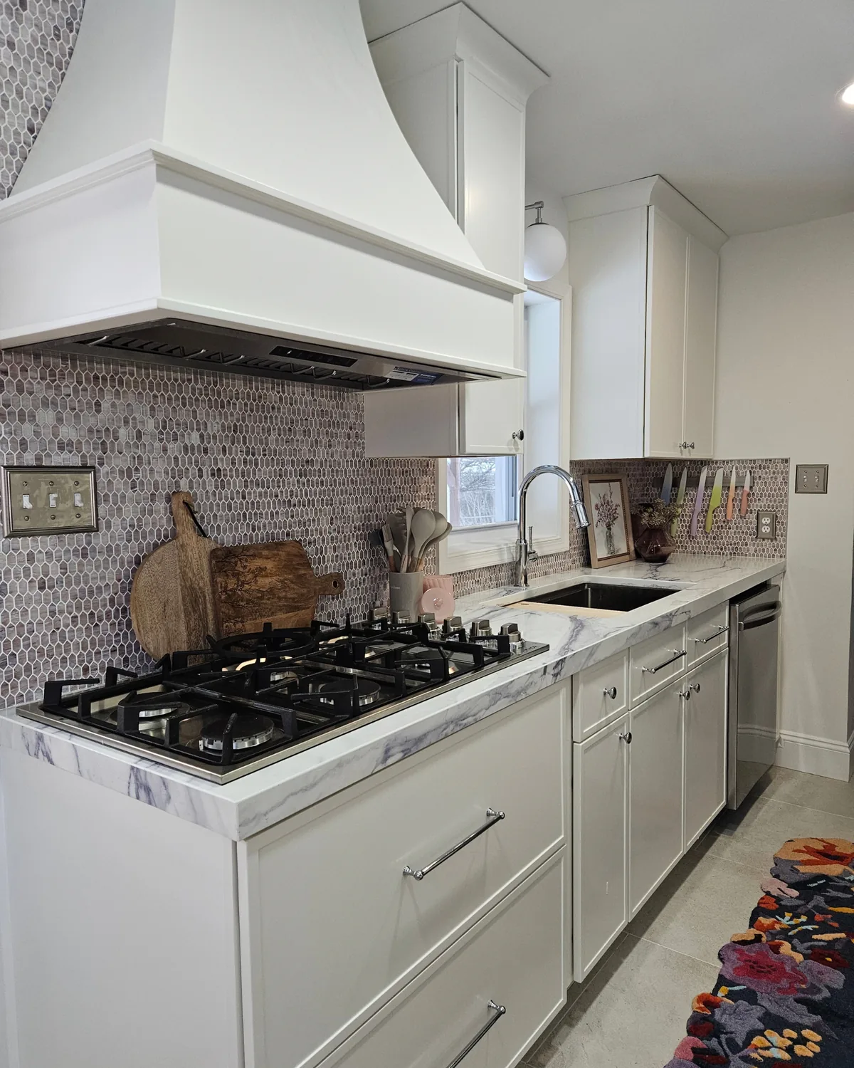 Gas cooktop and cream drawers along a marble counter, with a colorful floral runner on the floor