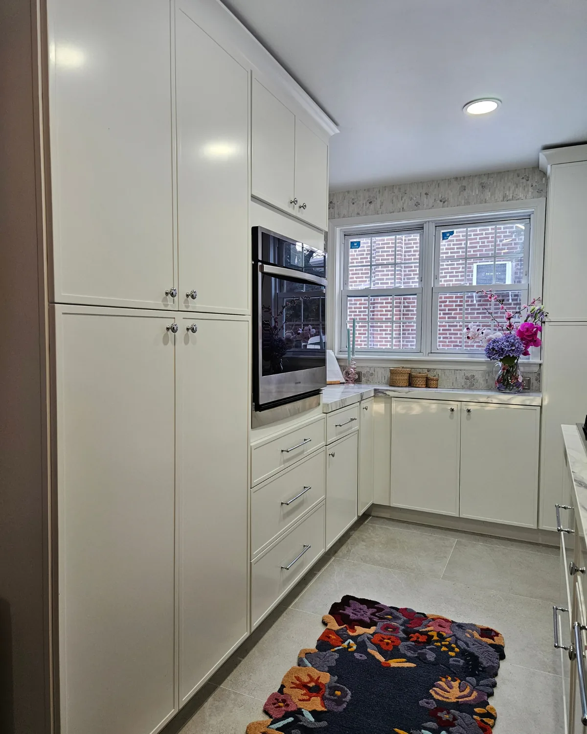 Kitchen view with cream cabinets, a wall oven and a navy floral runner on pale tile floors