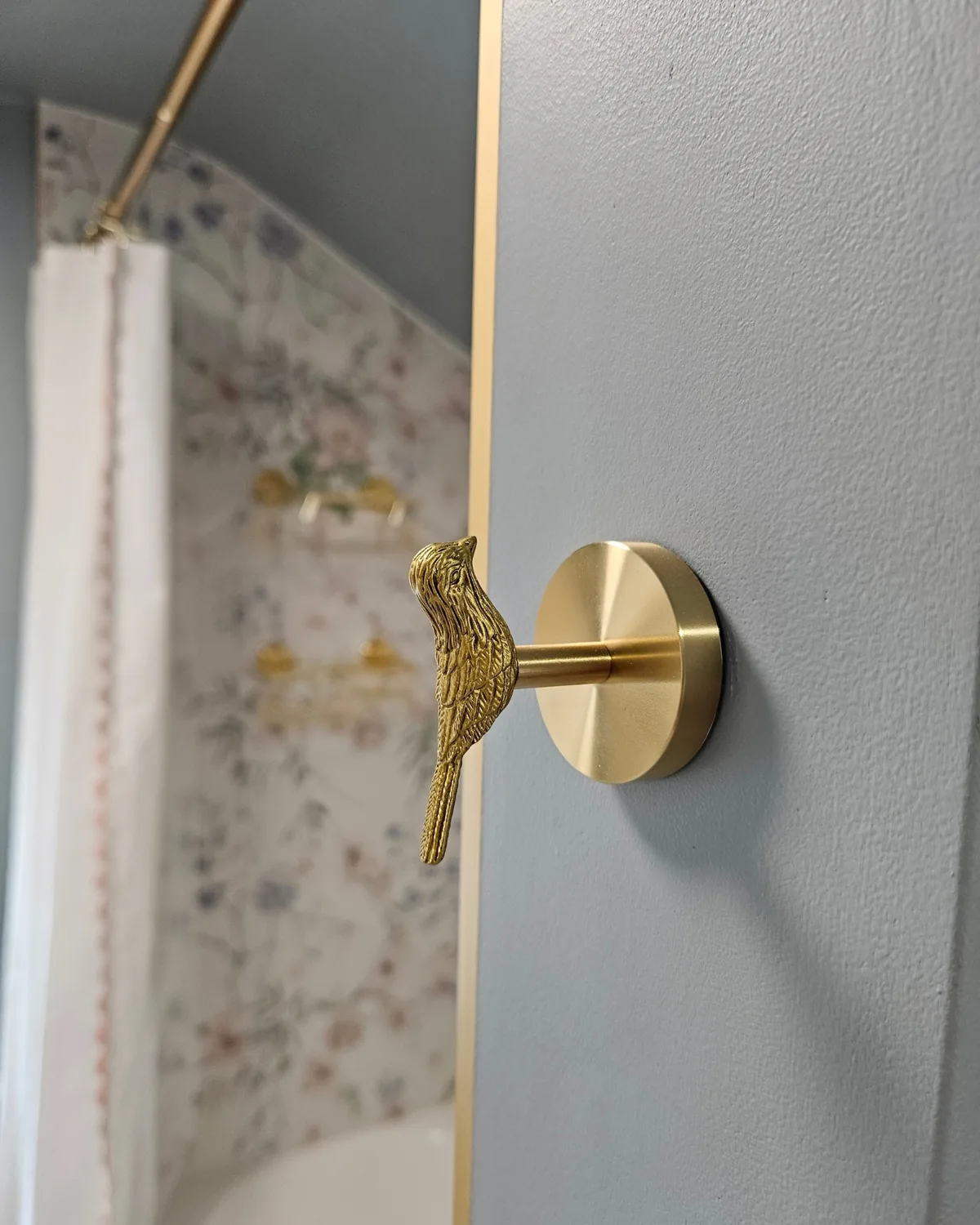 Brass bird-shaped hook on a blue-gray wall beside the floral tub tile