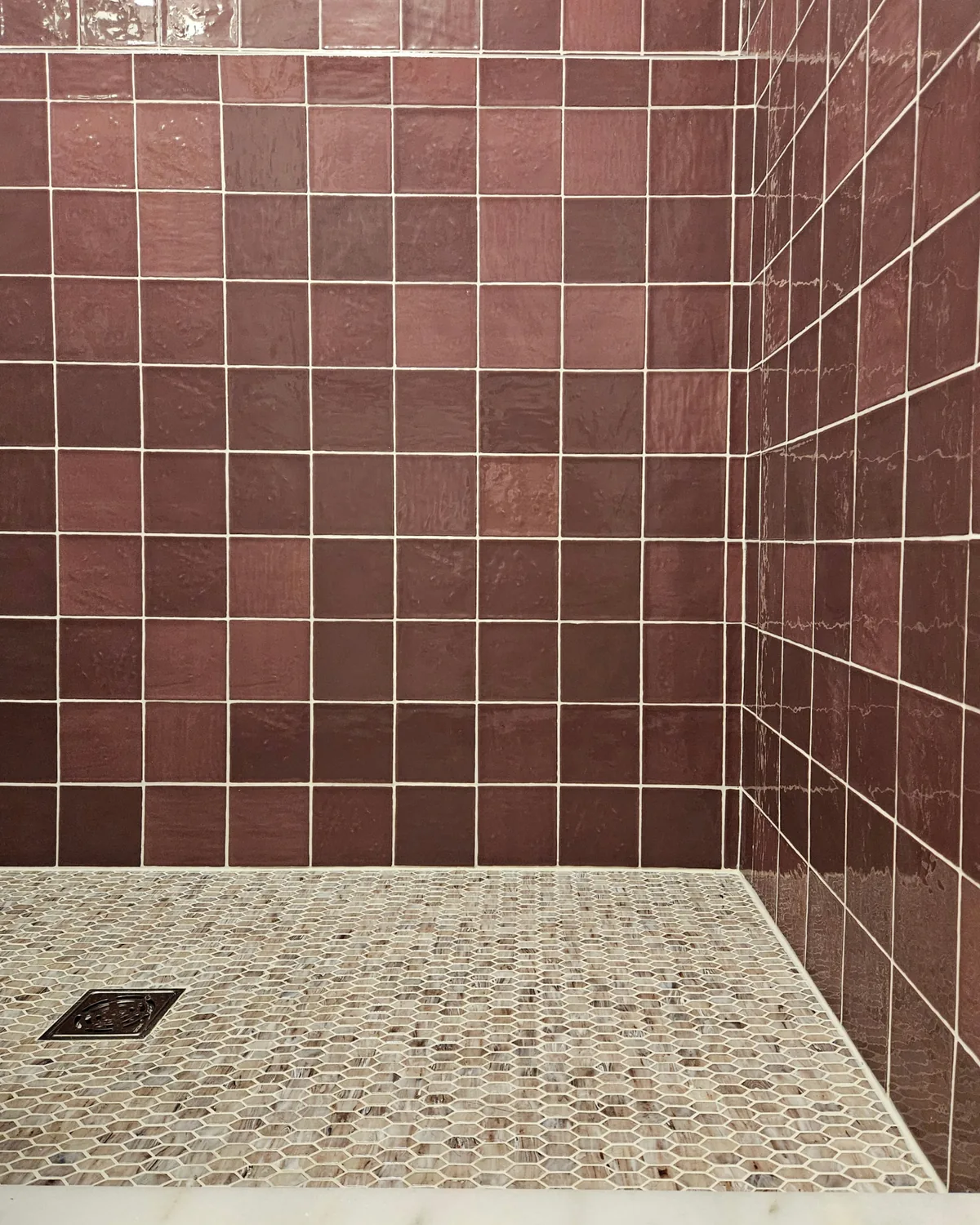 Walk-in shower with berry-red square tile and a pale pebble mosaic floor