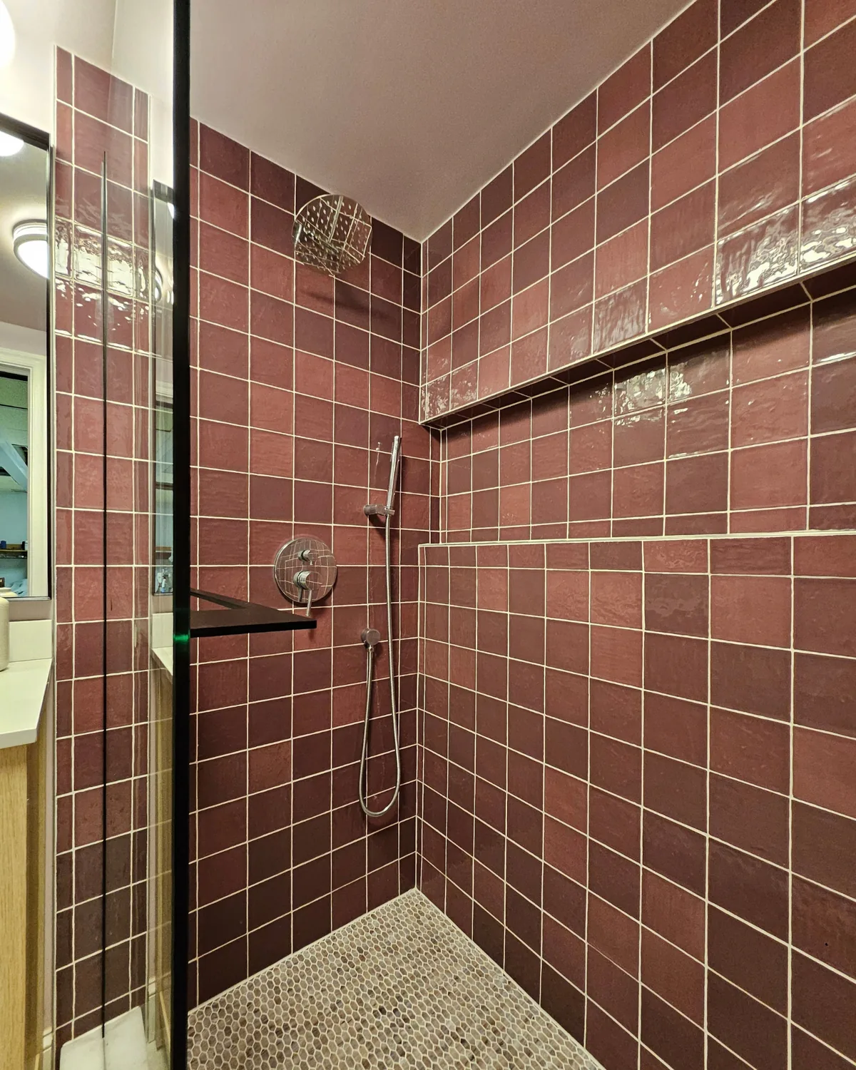 Glass-door shower with berry-red tile, a long niche and a rain showerhead