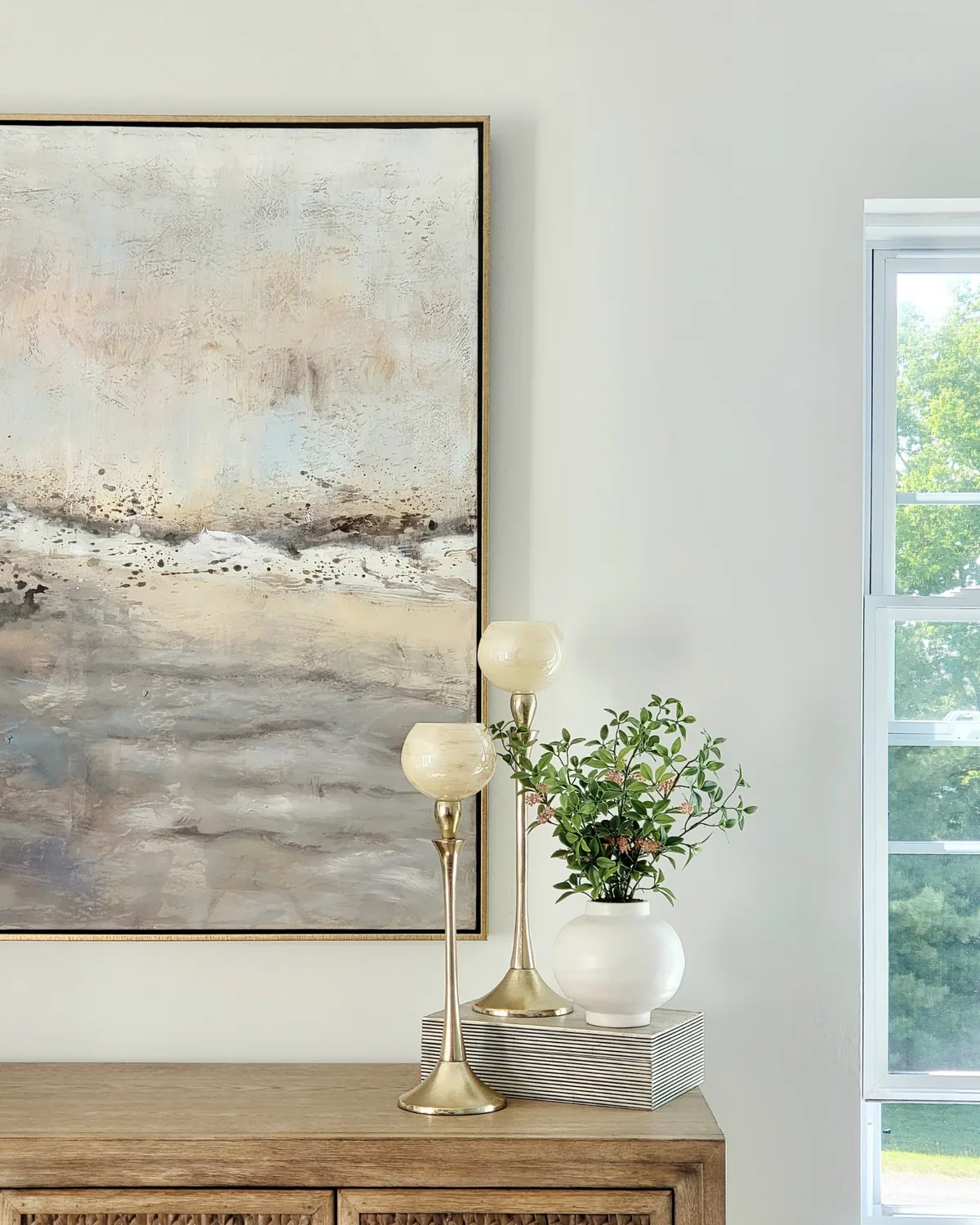 Close-up of the sea-toned abstract painting with brass candlesticks and a white vase of greenery