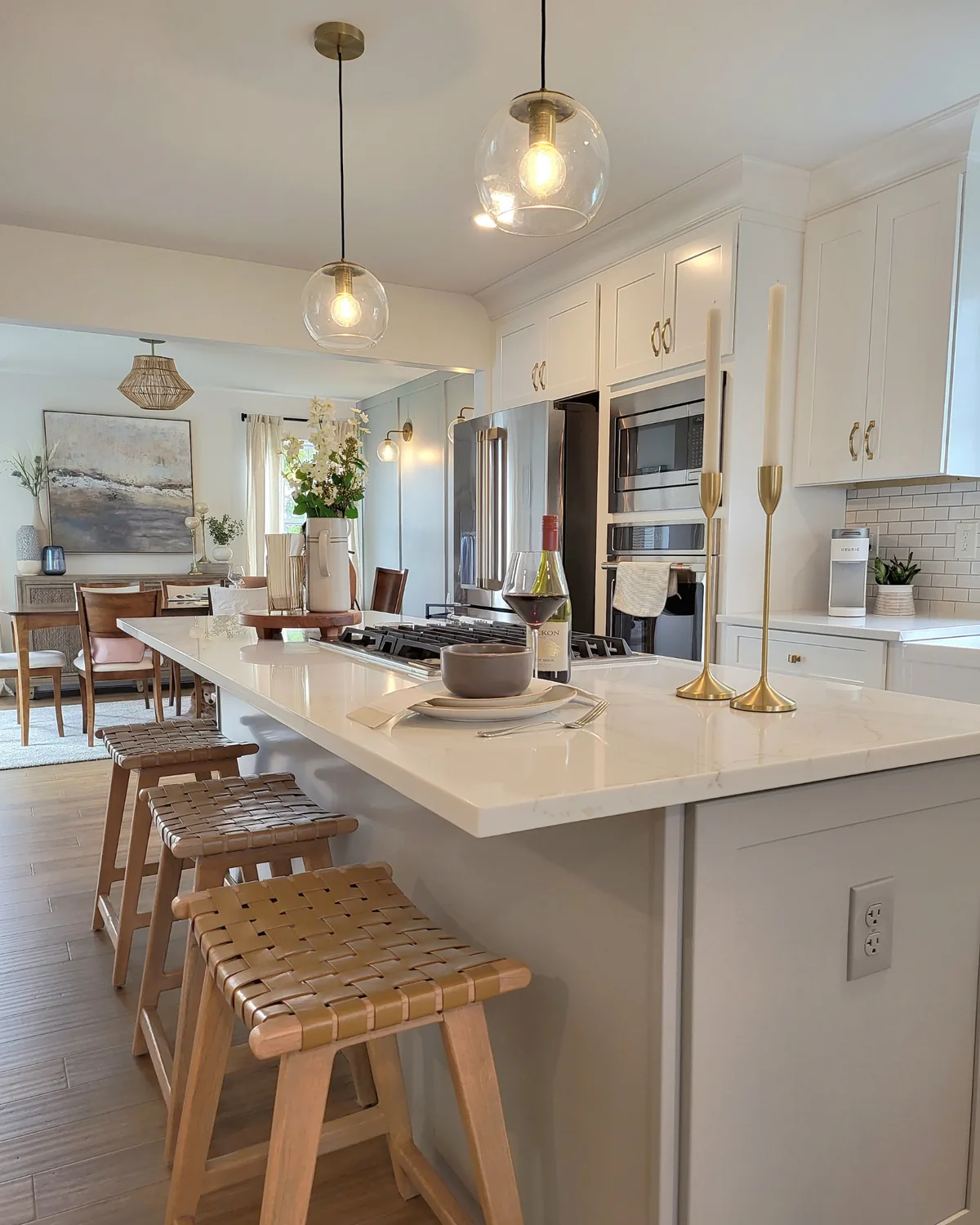 White kitchen island with leather-strap counter stools, glass globe pendants and brass candlesticks, opening to the dining room