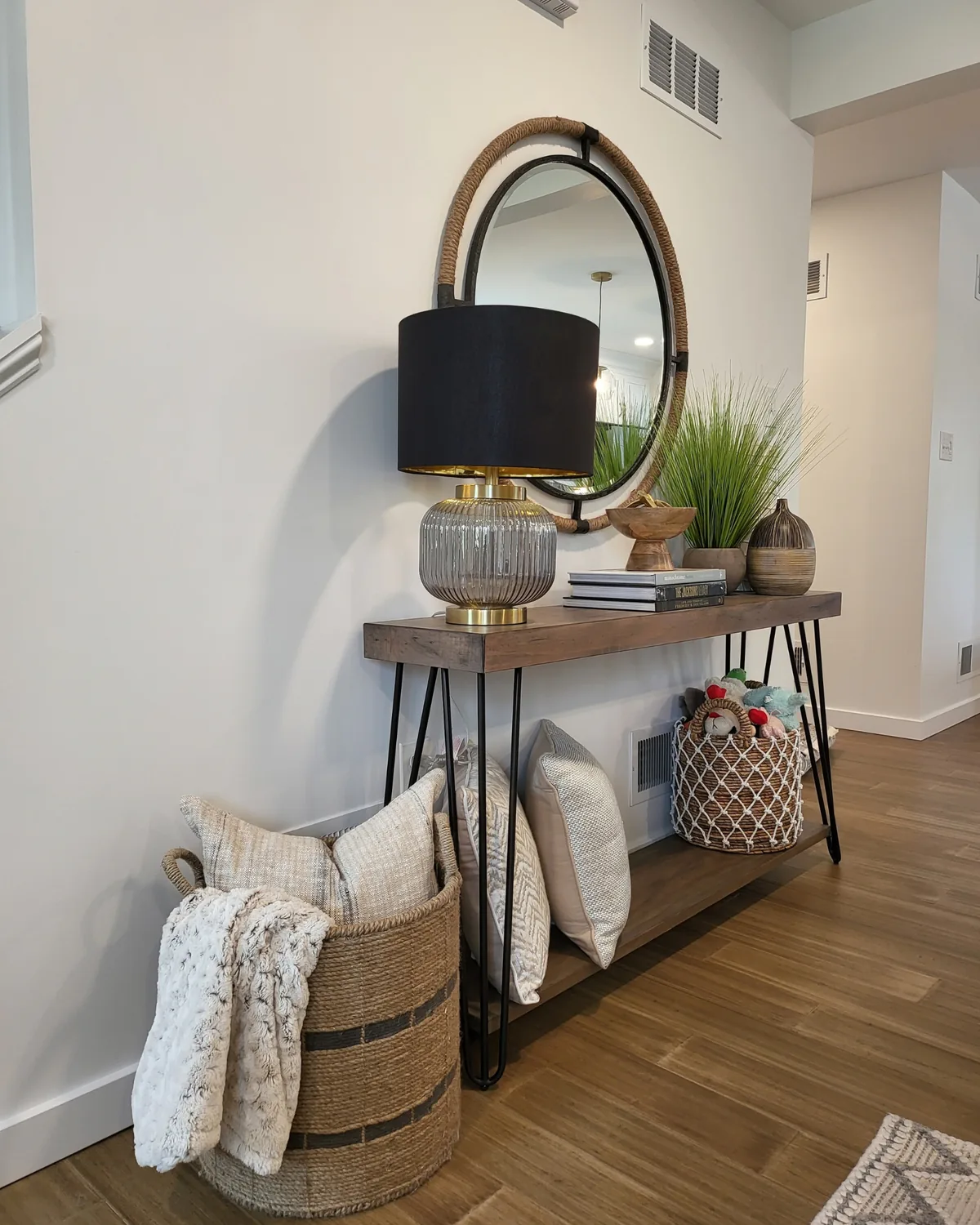 Entry console with a black-shaded lamp, a round rope mirror and baskets of pillows and throws