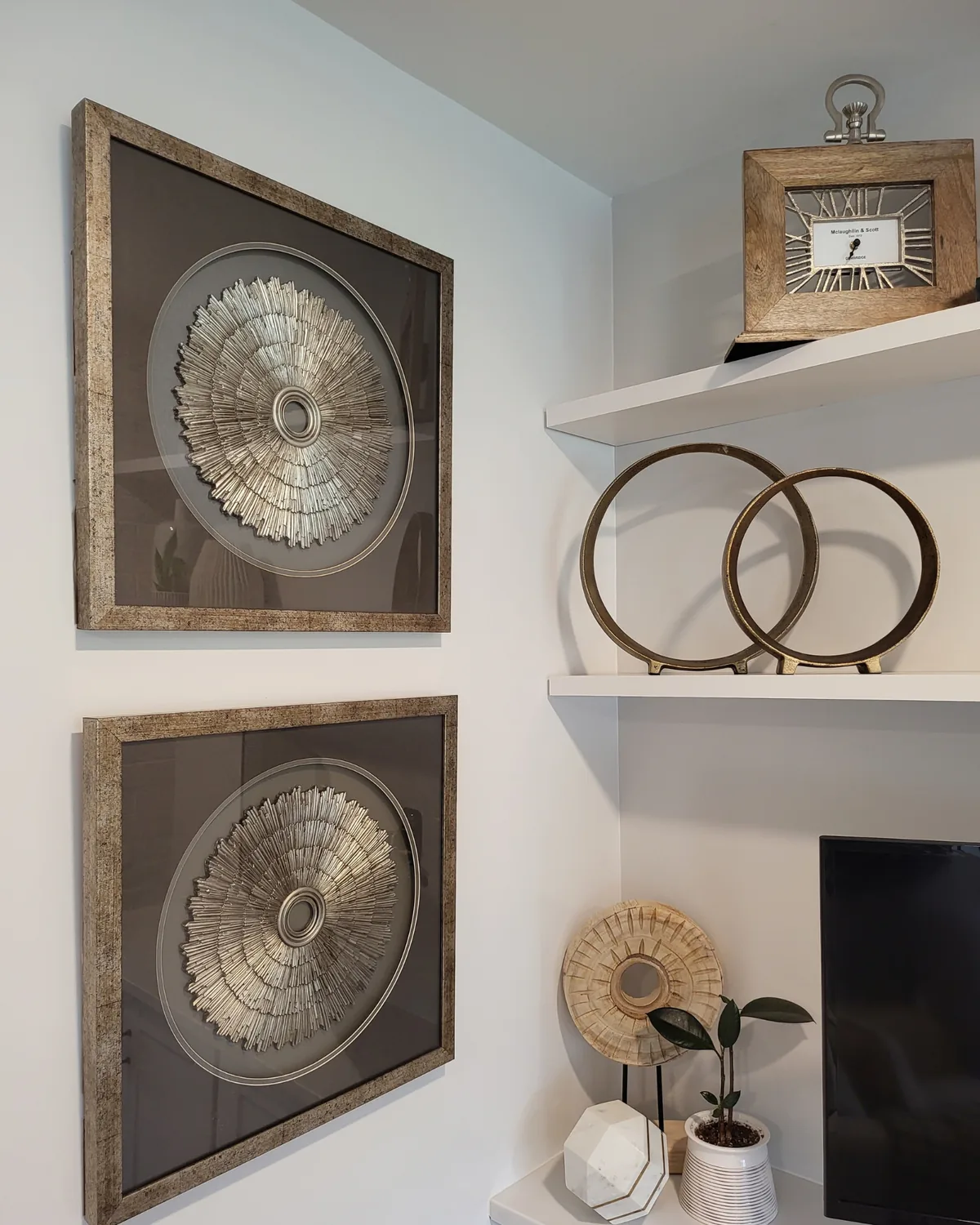 Framed silver medallion art beside open white shelves styled with brass rings and a vintage clock