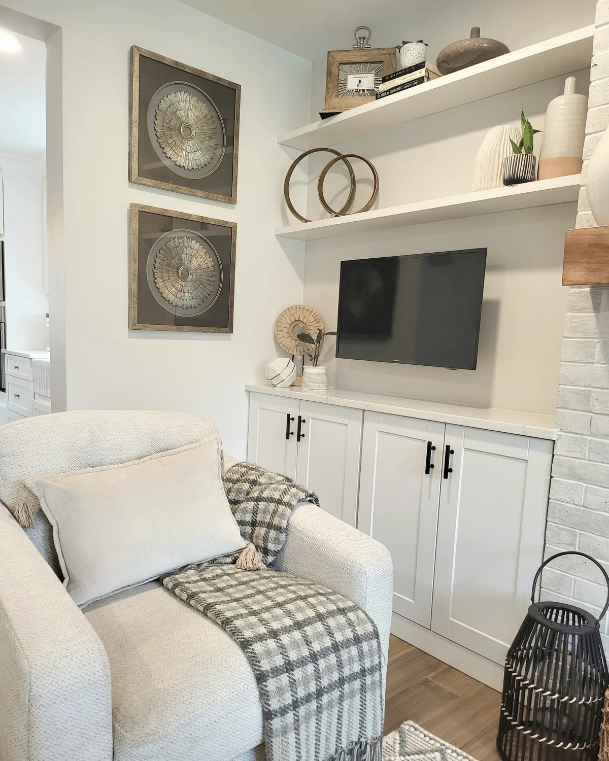 Living room corner with a cream armchair and plaid throw beside built-in shelves, cabinets and a wall-mounted TV