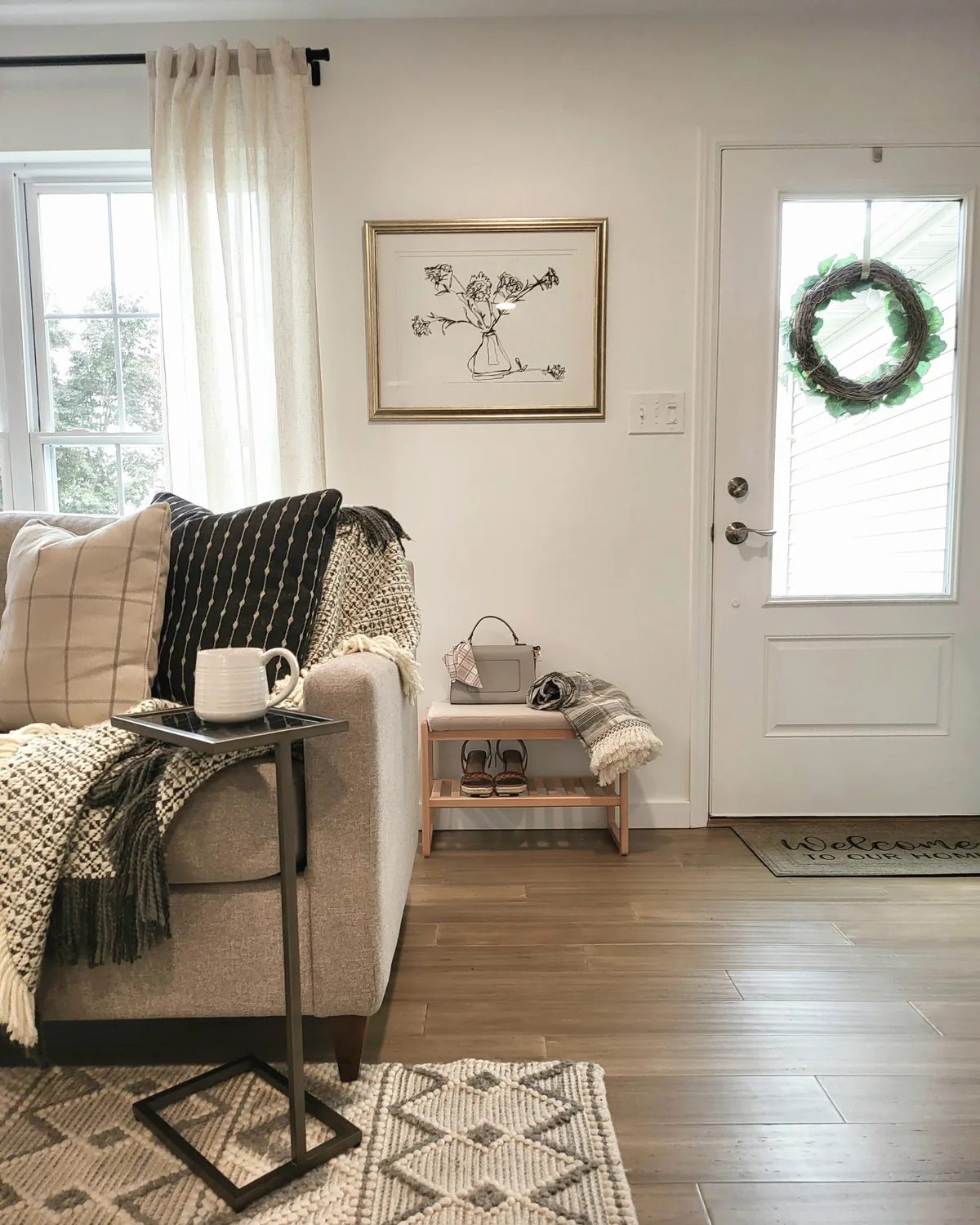 Sofa with black and cream pillows and a C-table near the front door, with a shoe bench and wreath