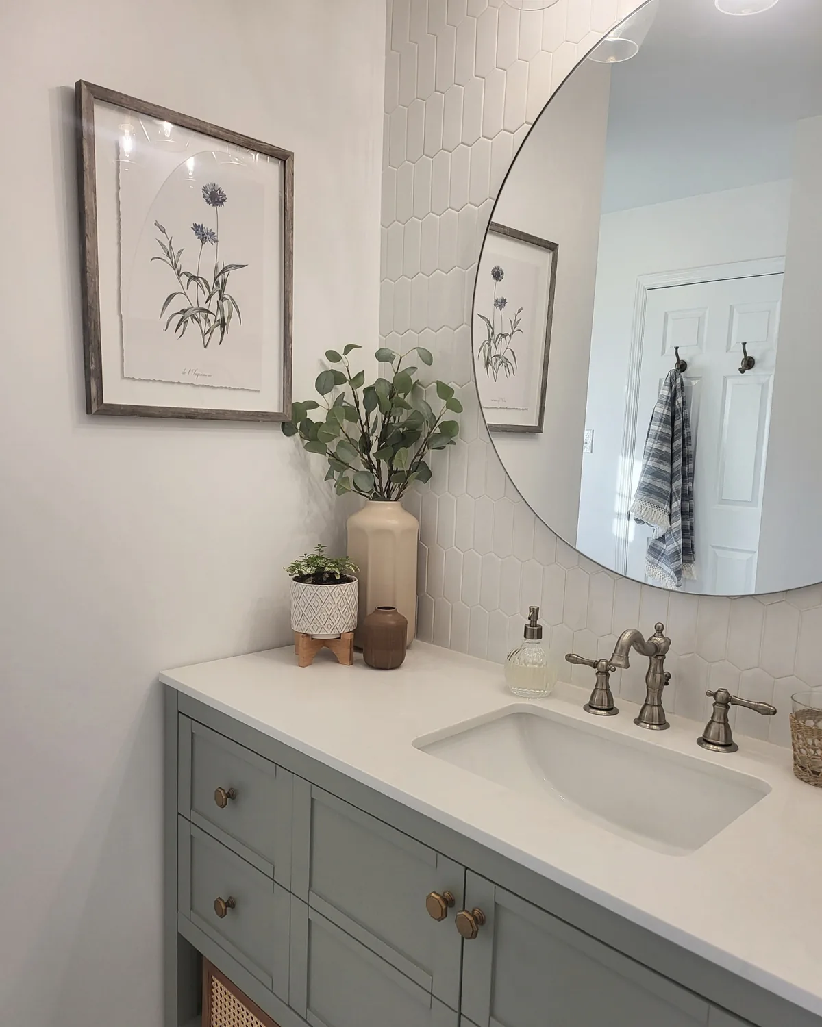 Sage green bath vanity with cane drawers, a round mirror, bronze faucet and white picket tile