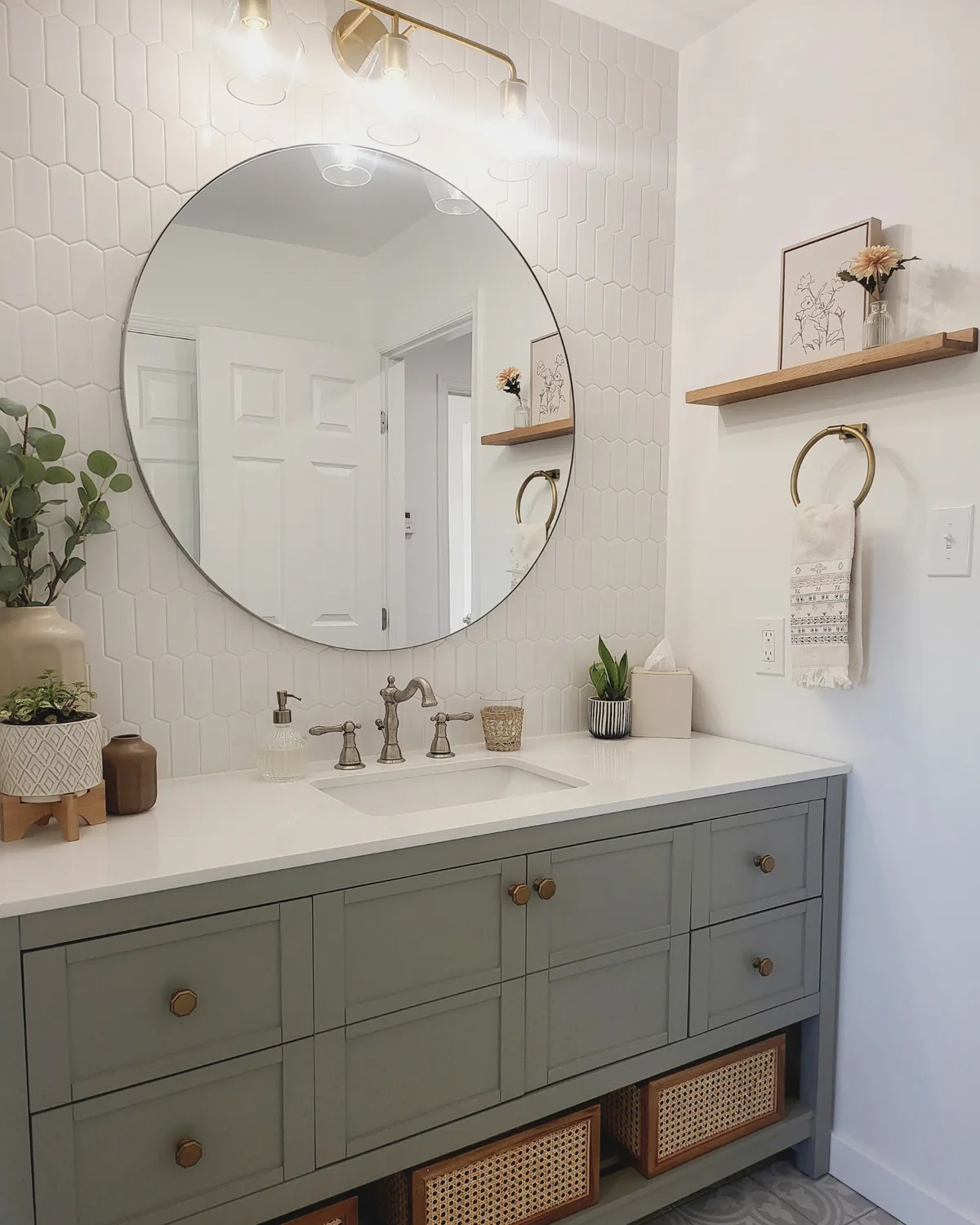 Full view of the sage vanity with cane baskets, a brass sconce, round mirror and floating wood shelf