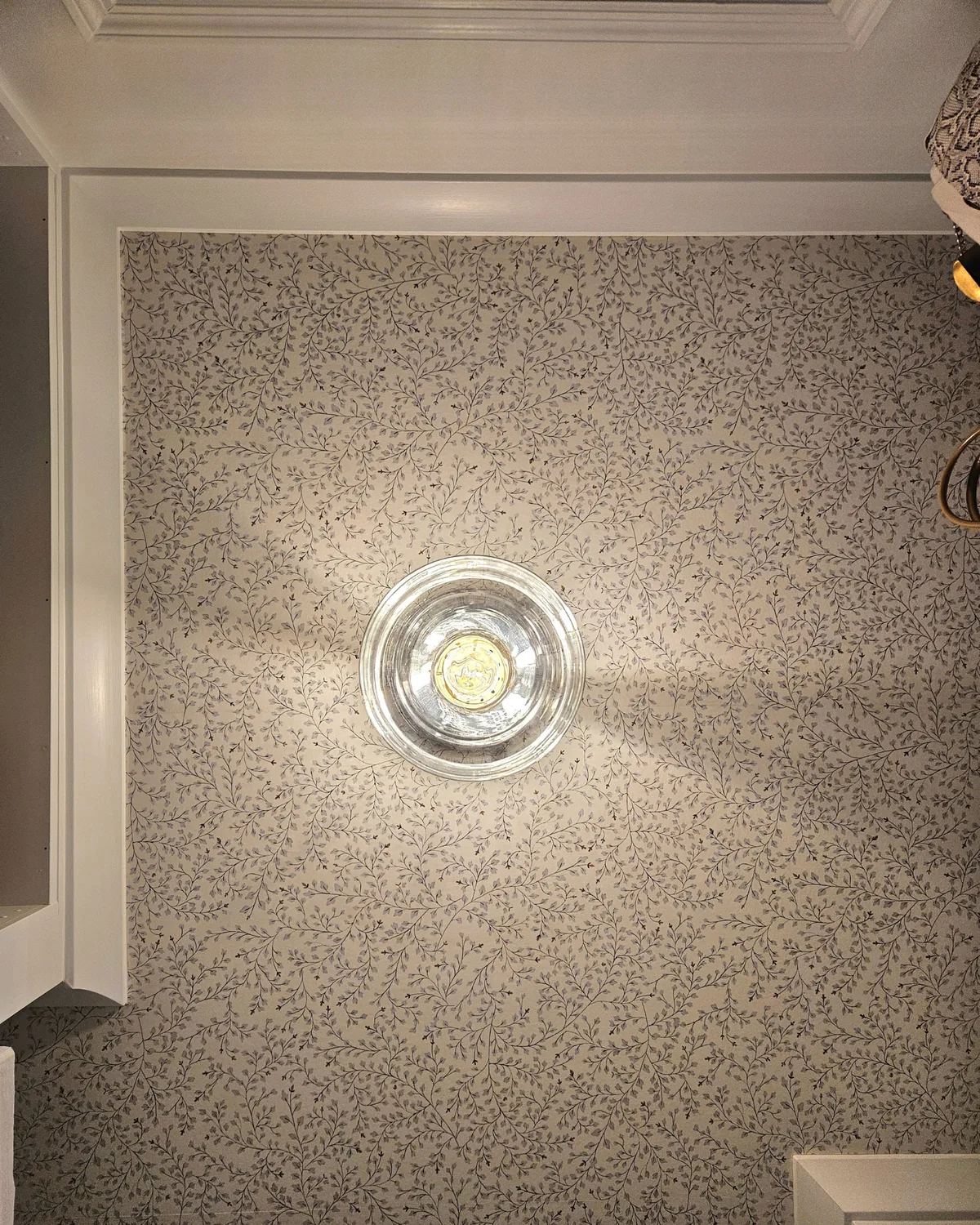 Looking up at the closet's speckled wallpapered ceiling and glass flush light